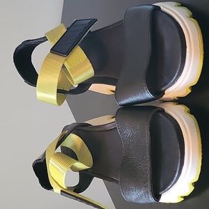 Women's Sorel sandal. Black leather upper, white lug sole, neon green accents.